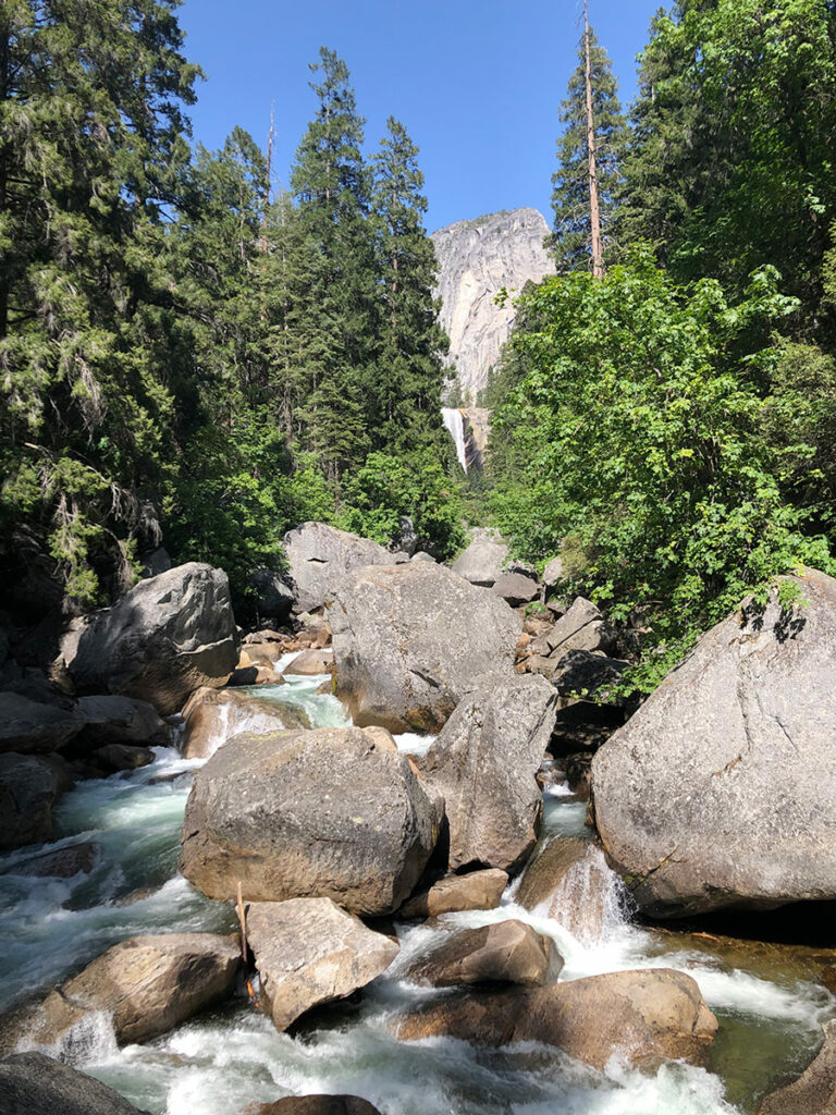View from Vernal Fall Footbridge. Rocks in foreground, waterfall in background.